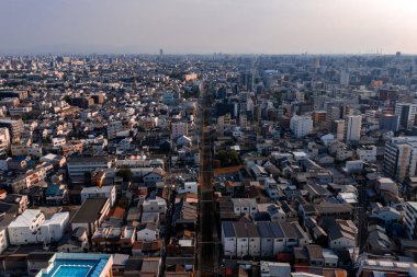 Japonya, Osaka 'nın puslu öğleden sonrası görüntüsü. Merkezde bir demiryolu hattı var, alçak ve orta bloklar çerçeveyi dolduruyor, yeşil bir tümsek düzgün duruyor, kuleler yükseliyor..