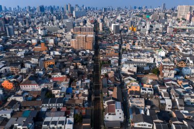 Hava manzarası, alçak katlı evlerin arasından Osaka yüksek binalarına doğru düz bir demiryolu hattı gösteriyor. Açık gün ışığı, kılavuz gibi blokları, temiz çizgileri ve ince ön cephe renklerini ortaya çıkarır.
