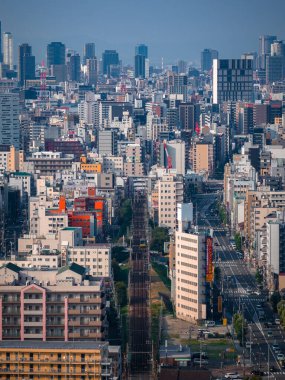 Merkez Osaka, Japonya, yukarıdan bakıldığında yoğun orta ve yüksek binalarda demiryolu hatları ve geniş yollar, ufukta modern kuleler, açık gündüz ışığı ve ızgara benzeri şekiller görülüyor..