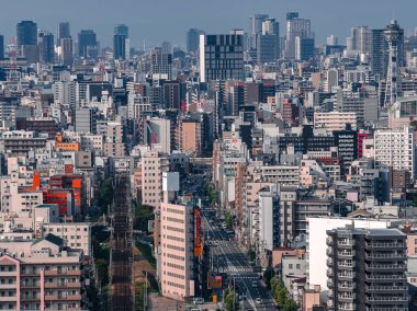 Japonya, Osaka 'nın hava manzarası, yoğun kuleler, demiryolu hatları ve geniş yollar gösteriyor. Tsutenkaku sağa doğru yükseliyor, Osaka Kalesi ortaya oturuyor, gün ışığı ve net bir detay..