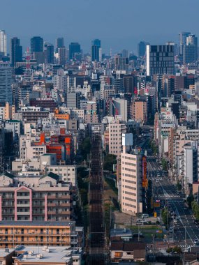 Japonya 'nın Osaka şehir merkezinin havadan görünüşü, yoğun orta ve yüksek binaların ortasından geçen bir demiryolu koridoru, açık gün ışığı, derin telefoto sıkıştırması ve gelişimi işaret eden vinçler..
