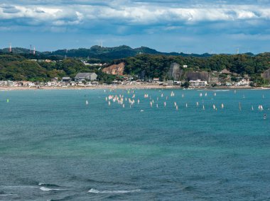Düzinelerce küçük yelkenli, turkuaz suyu noktalarken dalgalar kumlu Kamakura kıyılarına, alçak katlı kasabalara ve orman tepelerine doğru süzülüyor. Gündüz vakti bulutlar bir yelkenli yarışı öneriyor.