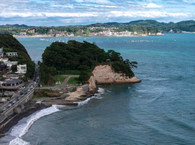 Kamakura, Japonya 'nın hava manzarası kayalık bir burnu, soluk bir kumtaşı uçurumunu, küçük bir körfezi, hafif trafiği, sıkışık evleri ve uzak yelkenli teknelerini gösteriyor..