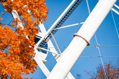 Yakından bakıldığında Riga 'daki dev bir dönme dolabın beyaz kirişleri, kabloları ve cıvataları görülüyor. Parlak gün ışığında turuncu sonbahar yapraklarıyla çerçevelenmiş, temiz çizgiler ve doymuş renklerle..
