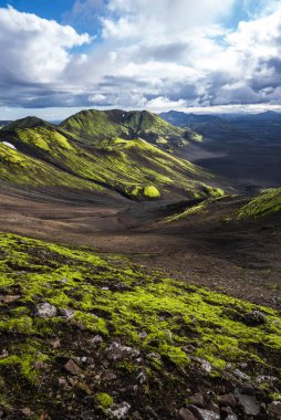 İzlanda, Landmannalaugar yakınlarındaki volkanik tepeler ve kül tarlaları, öğleden sonra geç saatlerde yosun dokularını, dalgalanan vadileri ve uzak sisli dağları ortaya çıkarıyor..