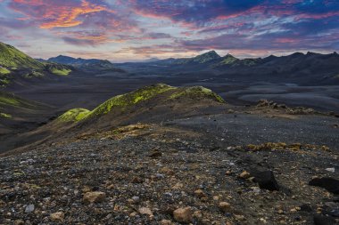 Karanlık lav tarlaları ve kül ovaları İzlanda 'da yosun tepeleriyle buluşuyor. Düşük ışık, ryolit tepeler ve siyah kum vadileri üzerinde kontrast oluşturuyor. Kayalar parlayan bir ufka doğru yol alıyor..