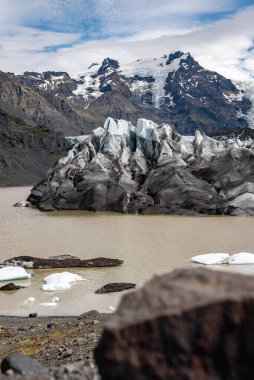 Koyu küllü mavi yarıklar İzlanda 'daki Vatnajokull Ulusal Parkı' nda bulunan çökelti zengini bir lagünle buluşuyor. Buz kütleleri siyah bir kumsalda sürükleniyor. Gün ışığı bulutlarının altında..