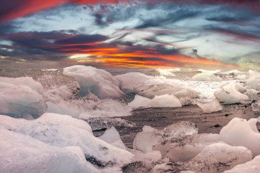 Jagged Ice, Diamond Beach, Jokulsarlon, İzlanda 'da dalgalar gibi siyah kumun üzerinde duruyor. Alacakaranlık ışığı, kışın kırmızı turuncu bulutlar oluşturur..