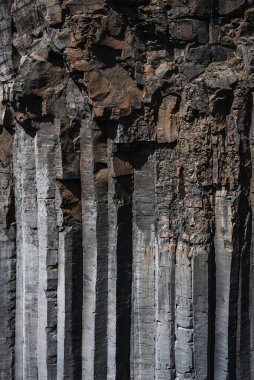 Uzun bazalt sütunlar İzlanda 'da bir uçurumda altıgen kuyular oluşturur. Sert yan ışık çatlakları ve pas çizgilerini tanımlar. Katmanlı volkanik kayaları ve keskin geometriyi ortaya çıkarır..
