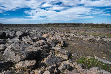 Geniş lav ovası, pürüzlü bazalt kayalar ve İzlanda 'da seyrek yosun. Gün ortası ışığı, koyu kayalar ve mavi ve beyaz bulutlar arasında kıtır kıtır gölgeler bırakır..