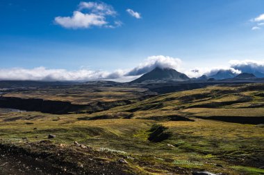 İzlanda 'nın Landmannalaugar yakınlarındaki iç kesimlerinde gün ışığı manzarası, yosunlu lav alanları düşük bulutlu, uzun gölgeli, yüksek kontrastlı, uçsuz bucaksız negatif uzayı olan konik bir zirveye götürür..