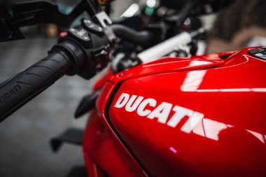 Parlak kırmızı Ducati yakıt deposu, kalın Ducati harfleri ve kapalı bir atölye veya garajda dokulu tutuşu, yumuşak odaklanma araçları, sığ alan derinliği, dramatik ışıklandırma.