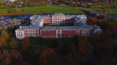 Düşük hava aracı görüntüsü Jelgava, Letonya 'daki Jelgava Sarayı' nı gösteriyor. U şekli, merkez avlu, Lielupe Nehri, köprü, gezinti güvertesi, park edilmiş arabalar ve sonbahar rengi..