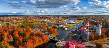 Lielupe ve Driksa nehirleri, beyaz yüksek binalar, yaya köprüleri ve kümülüs bulutları altında sonbahar renkleriyle Jelgava, Letonya 'nın öğleden sonra manzarası.