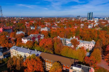 Riga, Letonya 'nın sonbahardaki hava manzarası. Altın kırmızısı ağaçlar tarihi villaları ve alçak blokları çevreleyecek, sağ tarafta Z kuleleri açık gün ışığında.