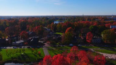 Uzun yansıtıcı gölü, kırmızı ve turuncu ağaçları, alçak evleri, dolambaçlı caddeleri, kilise kuleleri ve gün ışığının altındaki bacaları olan bir Riga şehir parkı..