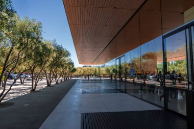 Yüzen çatısı olan cam pavyon Cupertino 'da zeytin ağaçlarının geçidi. Geniş açı, yansımaları ve insanları gösteriyor. Şirket kampüsünde parlak bir gün ışığı..