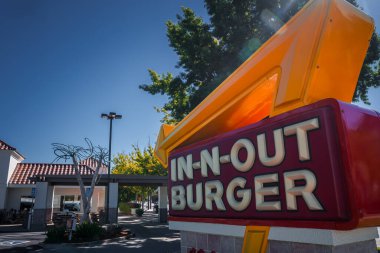 Santa Cruz 'da sarı oklu Burger tabelasını kapatın, açık mavi gökyüzü ve gölgeli ağaçlar, kırmızı kiremit çatılı beyaz binalar, açık gün ışığı ve gölgeler.