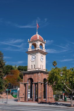 Santa Cruz Saat Kulesi Kaliforniya 'da sakin bir kavşakta duruyor. Yapraklı ağaçlar, alçak tepeler ve parlak gün ışığı altında bir Amerikan bayrağı..