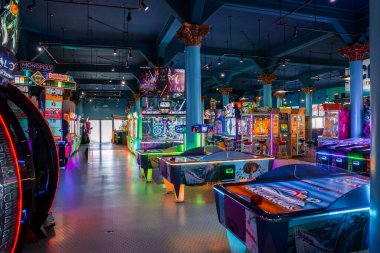 Santa Cruz, Kaliforniya 'daki kapalı oyun salonunda neon oyun dolapları, hava hokeyi ve deniz mavisi sütunları gösteriliyor. Açık kapıdan sahile doğru yol alırken çok az ziyaretçi görünür..