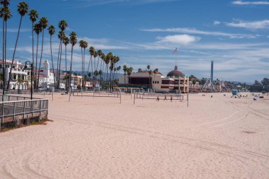 Palmiye ağaçları, hindistan cevizi koruluğu ve Santa Cruz, Kaliforniya 'da gezintileri olan geniş kumlu bir sahil. Gün ortası ışığı, seyrek kalabalık, voleybol sahası ve gezinti alanı boş zamanı öneriyor..