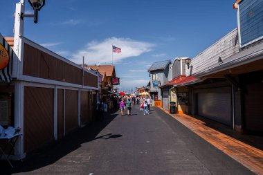 Ziyaretçiler gün ortasında Monterey 'deki Old Fisherman' s Wharf boyunca deniz ürünleri barakaları, hediyelik eşya dükkanları, bir Amerikan bayrağı ve marina yakınlarında uzak bir atlıkarınca ile geziyorlar..