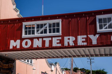 Monterey, Kaliforniya 'da Monterey' de Monterey Row 'da bulunan koyu kırmızı yaya köprüsü, kiremit çatıları ve elektrik direkleriyle aydınlık gün ışığında çerçevelenmiş..
