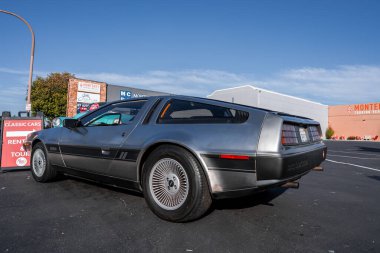 Paslanmaz çelikten bir DeLorean DMC 12 Monterey, Kaliforniya 'da park halinde, alçak arka üç çeyrek açılı, hoparlörlü arka pencere ve türbin tekerlekleriyle görülüyor..