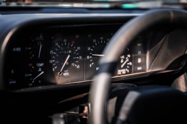 DeLorean DMC 12 'deki analog hız göstergesini kapat, siyah bir kümede takometre, sıcaklık ve volt, sıcak öğleden sonra ışığı, Monterey, California, klasik araba ekranı.