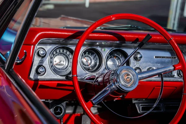 Monterey, California 'da klasik bir Amerikan arabasının içini kapatın. Kırmızı direksiyon ve krom göstergeler arasında hız göstergesi, yakıt göstergesi ve parlak gün ışığında saat yer almaktadır..