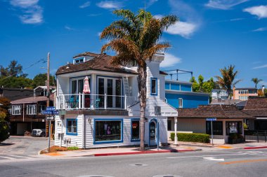 Capitola 'nın başkenti Capitola' da Monterey Bulvarı 'ndaki bir sahil mağazasının güneşli gündüz manzarası, bir taret, palmiye, balkon sandalyeleri ve pembe bir şemsiyesi var..