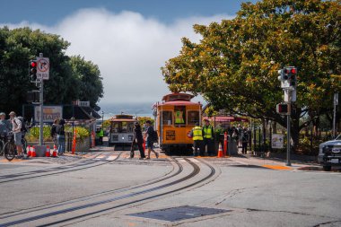 Parlak turuncu teleferikler, San Francisco rıhtımındaki Powell Hyde dönüşünde duraklıyor. Yolculara rehberlik eden ve gün ortasında rayları birleştiren görevlilerle birlikte..