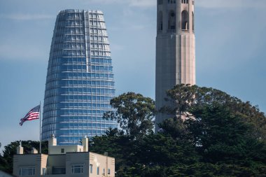 San Francisco silueti, Satış Gücü Kulesi 'nin solda, Coit Kulesi' nin sağda olduğunu gösteriyor. Açık bir çatıda Amerikan bayrağı dalgalanır, Telegraph Hill 'de ağaçlar, açık gün ışığı..