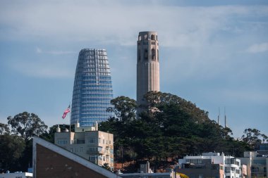 Telegraph Hill 'deki Coit Kulesi San Francisco, Kaliforniya' daki Satış Gücü Kulesi 'nin önünde duruyor. Evler, ağaçlar ve bir Amerikan bayrağı yumuşak, hatta gün ışığında belirir..