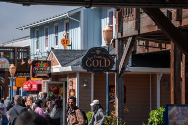 Kalabalık renkli ahşap mağazaların önünden geçiyor ve San Francisco, California 'daki 39. İskele' de parlak öğlen ışığı altında canlı gölgeler ve neşeli bir ruh hali içinde asılı tabelalar var..
