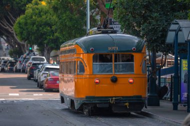 Yeşil ve turuncu PCC 1071 San Francisco caddesi boyunca yola çıkıyor, arabalar park halinde, sağda duruyor, hafif gün ışığı ve sisli, dikiz manzarası Art Deco kıvrımlarını vurguluyor.