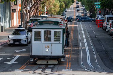 San Francisco, California, öğle vakti. Kablolu araba. Kondüktör ve yolcular, tramvaylar, park halindeki arabalar ve görünür tabelalarla, dik bir caddeye tırmanıyor..