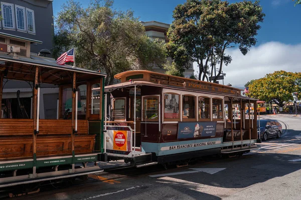 Powell ve Hyde 'ı işaretlemiş bir San Francisco teleferiği Kaliforniya' da bir kavşakta bekliyor, odun bankları, eski tabelalar, bayraklar, ağaçlar ve Viktorya dönemi aydınlığında binalar..