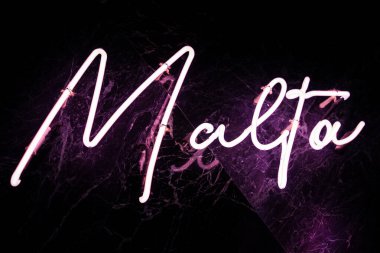 Parlak pembe neon işareti, Malta 'yı parlak siyah bir duvara karşı eflatun yansıtacak şekilde büyüler. Sıkı köşegen yapısı modern Malta 'da gece hayatı olduğunu gösteriyor..