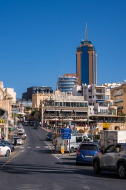 Sliema, Malta 'daki gündüz sokağı, Pordoso ve Mercury Towers ile St. Julian' s ufuk çizgisine kadar yokuş yukarı görünüyor. Kafeler, trafik ve yayalar parlak ışıkta kıyı şeridi oluşturuyorlar..