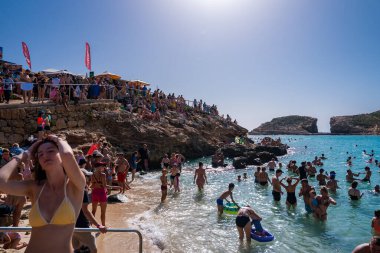 Yüzücüler ve güneş banyosu yapanlar Malta 'nın Comino Adası' ndaki Mavi Göl 'ü dolduruyorlar. İnsanlar gün ışığında güneşli kayaların altındaki teraslarda yürüyor, yüzüyor ve dinleniyorlar..