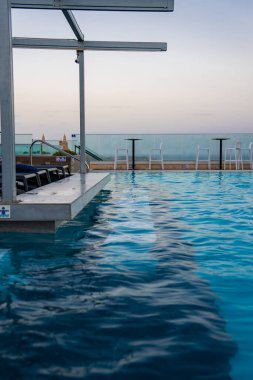 Sonsuz çatı, akşam üzeri Mellieha Malta 'da tabure ve masalarla dolu cam bir balyoza bakar. Comino ve Gozo' ya doğru manzaralı, şezlonglar ve bir cankurtaran şamandırası..