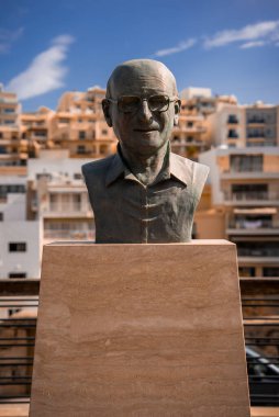 Gözlüklü bronz bir büst Mellieha, Malta 'da parlak bir kaide üzerine oturur. Gündüz sığ derinliği, katmanlı kireçtaşı daireler ve balkonlarla ilgili detayları izole eder..