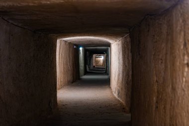 Mellieha Malta 'da 2. Dünya Savaşı' ndan kalma uzun bir kireçtaşı sığınak tüneli kemerli tavanlar, tekrarlayan çerçeveler ve yumuşak yan ışık şeritleri ile parlak uzak bir açıklığa doğru çekiliyor..