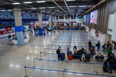 Luqa 'daki Malta Uluslararası Havaalanı' nın geniş bir iç manzarası var. Bavul, dükkan ve Costa Kahve kuyruğunda bekleyenler, parlak ışıklar ve cilalı yerler yoğun bir gün olduğunu gösteriyor.