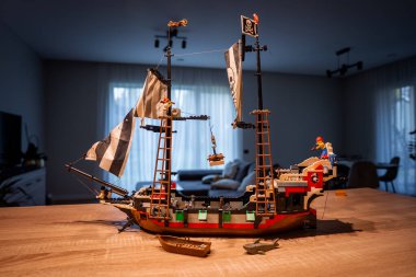 Bir LEGO korsan gemisi, yumuşak aydınlatılmış oturma odasındaki ahşap bir masada oturur. Minik incir korsanları teçhizata tırmanıyor, bir papağan tüneği, bir hazine kovası sallanıyor ve yakınlarda bir köpekbalığı dinleniyor..