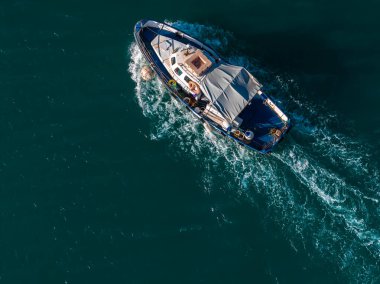Hava görüntüsü, Malta 'da bir Marsaxlokk balıkçı teknesinin deniz mavisi suda köpüklü bir şekilde ilerlediğini gösteriyor. Mavi gövde, güverte, halatlar ve şamandıralar gün ışığında görülebilir..
