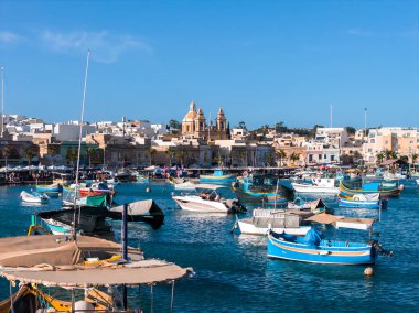 Marsaxlokk limanının gündüz görüşü, Malta, renkli luzzu tekneleri ve turkuaz su üzerindeki gemileriyle, ikiz çan kuleleri ve Pompei Leydisi 'nin kubbesi, pazar, ılık ışık kulesi.