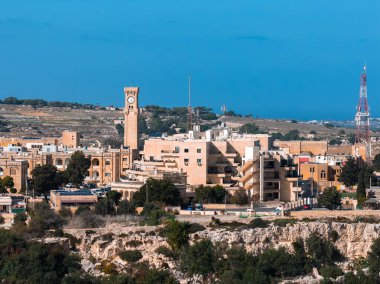 Mdina ve Rabat 'ın gündüz görüşü, Malta, kireçtaşı caddelerin üzerindeki saat kulesi, güçlendirilmiş duvarlar, kayalık arazi ve açık ışık altında soluk Akdeniz ufkuyla.