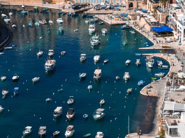 Sliema, Malta marinası havadan bakıldığında turkuaz suda küçük tekneler, eğimli taş rıhtımlar, basamaklar ve açık bir günde mavi tenteli kafeler görülüyor..